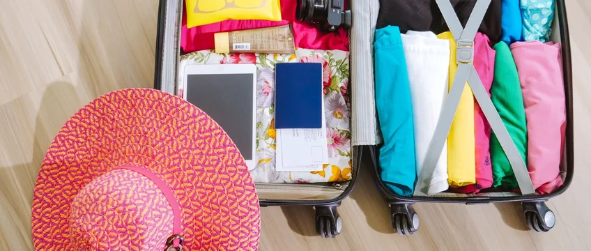 Open suitcase packed with clothes, a camera, sunglasses and a sun hat for a beach vacation